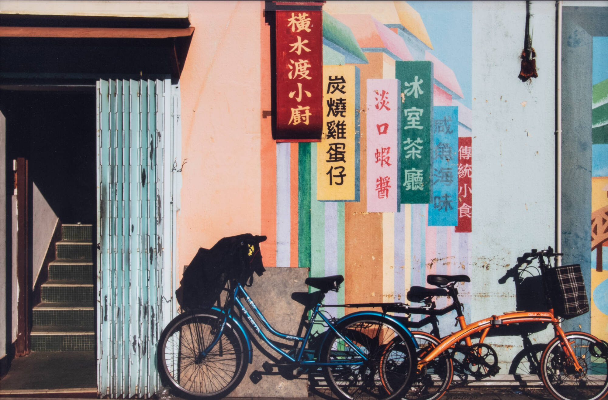 Color photograph of a street scene with a bicycle and mural of flags.